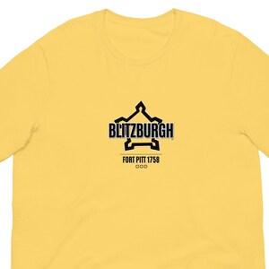 May include: A yellow t-shirt featuring a black graphic with the text "BLITZBURGH" above "FORT PITT 1758" and "000". The shirt is made of a soft material, with short sleeves and a crew neck.