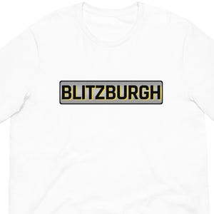 May include: White t-shirt with the word "BLITZBURGH" in a black and gold rectangular design across the chest. The shirt is made of a soft, comfortable material.