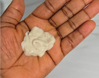 May include: A close-up of a hand holding a dollop of off-white, creamy substance. The substance appears to be thick and textured, with a slightly glossy sheen. The hand is open, and the substance is resting in the palm.