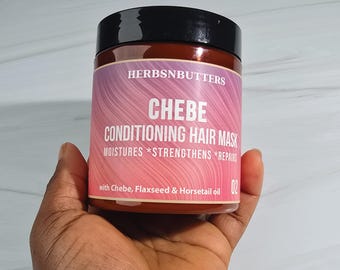 May include: A jar of CHEBE Conditioning Hair Mask by HERBSNBUTTERS. The jar has a black lid and a label with a pink and purple gradient. The label states the product moisturizes, strengthens, and repairs hair, and contains Chebe, Flaxseed & Horsetail oil.