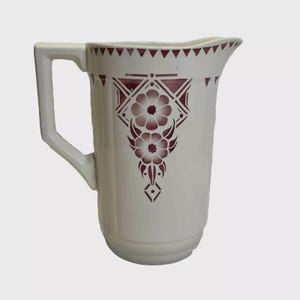 Peut inclure: Pichet en céramique blanche avec une anse rectangulaire et un bec verseur. Il est orné d'un motif floral bordeaux et de motifs géométriques sur le bord. Un objet décoratif pour servir des boissons.