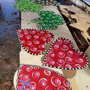 May include: A collection of wooden heart-shaped door hangers with a black and white trim. The hearts are painted red with white and pink swirls. One heart has the word "love" written in purple.