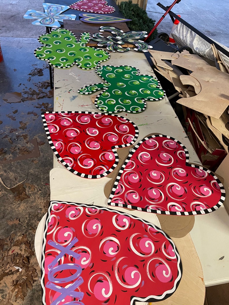 May include: A collection of wooden heart-shaped door hangers with a black and white trim. The hearts are painted red with white and pink swirls. One heart has the word "love" written in purple.