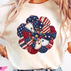 Peut inclure: Sweat-shirt ivoire avec un grand motif floral patriotique. La fleur est faite de tissu rouge, blanc et bleu avec des motifs d'étoiles et de rayures. Le centre de la fleur a une étoile dorée et de petits accents de perles. Le mot "IVORY" est imprimé en bas.
