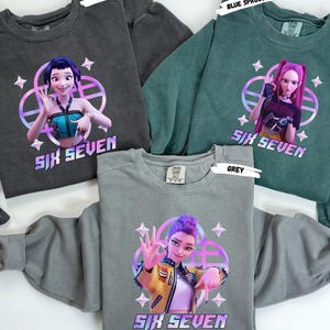 May include: Three crewneck sweatshirts in pepper, blue spruce, and grey. Each sweatshirt features a colorful graphic of a cartoon character with the text "SIX SEVEN". The sweatshirts have a vintage, washed look.