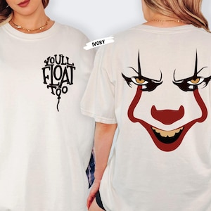 Op de afbeelding: Ivoor t-shirt met een zwarte ballonafbeelding en de tekst "You'll Float Too" op de voorkant. De achterkant van het shirt toont een rood en wit clowngezicht. Het shirt heeft een comfortabele, oversized pasvorm.