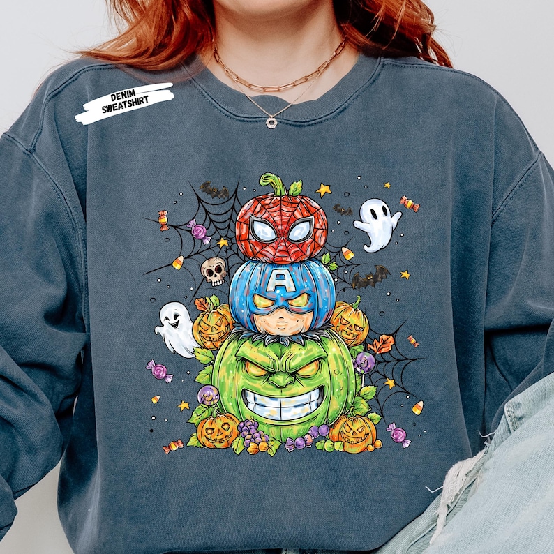 Puede incluir: Sudadera vaquera con dise&ntilde;o de Halloween. El gr&aacute;fico muestra tres calabazas apiladas, cada una con tem&aacute;tica de superh&eacute;roe: Spider-Man, Capit&aacute;n Am&eacute;rica y Hulk. Elementos de Halloween como fantasmas, caramelos y telara&ntilde;as.