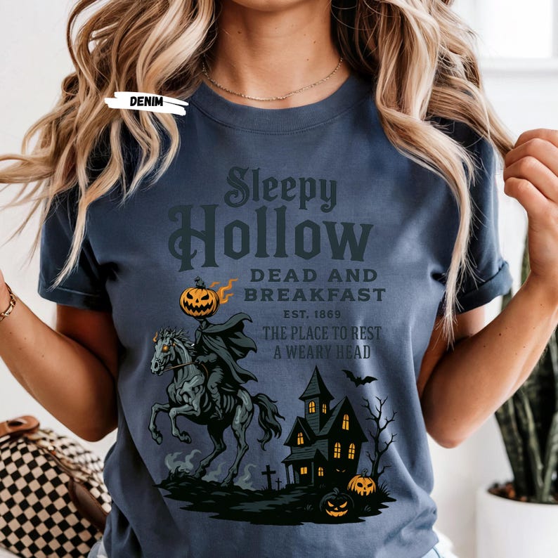 "Sleepy Hollow Halloween shirt featuring a vintage-style Headless Horseman on a spooky horse holding a jack-o'-lantern in front of a haunted house with glowing pumpkins and bats. This eerie Halloween graphic tee is printed on a moss green t-shirt and perfect for spooky season, trick-or-treat, horror movie lovers, gothic fall fashion, haunted house fans, or those searching for a unique October outfit. Ideal for fall events, pumpkin patches, or Halloween parties."