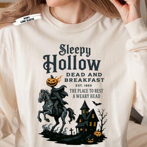 "Sleepy Hollow Halloween shirt featuring a vintage-style Headless Horseman on a spooky horse holding a jack-o'-lantern in front of a haunted house with glowing pumpkins and bats. This eerie Halloween graphic tee is printed on a moss green t-shirt and perfect for spooky season, trick-or-treat, horror movie lovers, gothic fall fashion, haunted house fans, or those searching for a unique October outfit. Ideal for fall events, pumpkin patches, or Halloween parties."