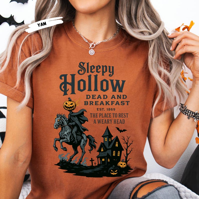 "Sleepy Hollow Halloween shirt featuring a vintage-style Headless Horseman on a spooky horse holding a jack-o'-lantern in front of a haunted house with glowing pumpkins and bats. This eerie Halloween graphic tee is printed on a moss green t-shirt and perfect for spooky season, trick-or-treat, horror movie lovers, gothic fall fashion, haunted house fans, or those searching for a unique October outfit. Ideal for fall events, pumpkin patches, or Halloween parties."