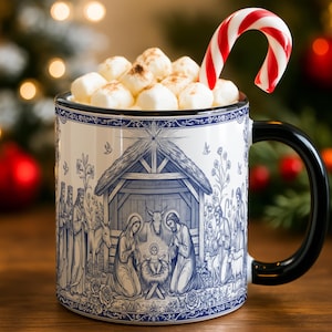 May include: A ceramic mug with a black handle and a blue and white nativity scene design. The mug is filled with marshmallows and a red and white candy cane. The text "MORE COLOR OPTIONS" is at the bottom.