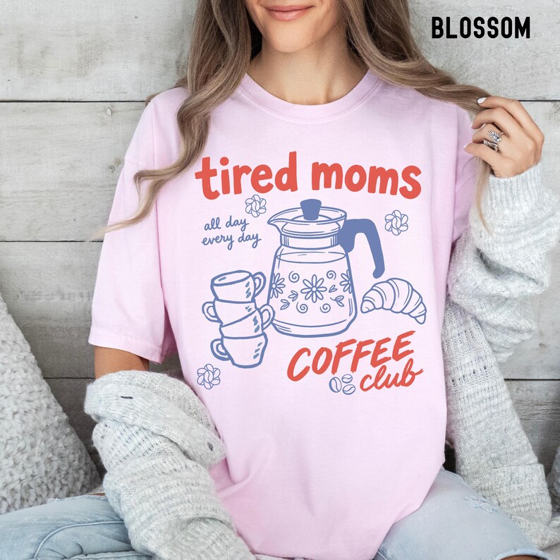 Vintage style graphic t-shirt featuring coffee pot, stacked cups, croissant, and playful tired moms coffee club text in soft pastel colors for moms. Printed on Comfort Colors t-shirt in Blossom.