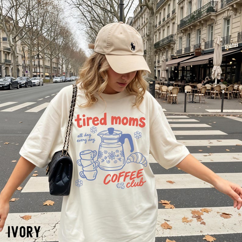 Vintage style graphic t-shirt featuring coffee pot, stacked cups, croissant, and playful tired moms coffee club text in soft pastel colors for moms. Printed on Comfort Colors t-shirt in Ivory.