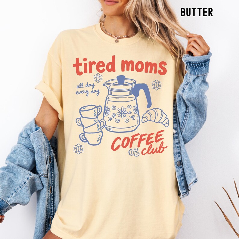 Vintage style graphic t-shirt featuring coffee pot, stacked cups, croissant, and playful tired moms coffee club text in soft pastel colors for moms. Printed on Comfort Colors t-shirt in Butter.