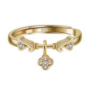 Könnte beinhalten: Ein goldfarbener, verstellbarer Ring mit einem Kleeblatt-Anhänger. Der Ring hat kleine, klare Edelsteine und den Text "S925". Der Ring hat ein dekoratives Design auf jeder Seite des Anhängers.