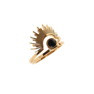 May include: A gold ring with a sunburst design and a black circular stone. The ring features a detailed, layered design with a central black stone, set against a white background.