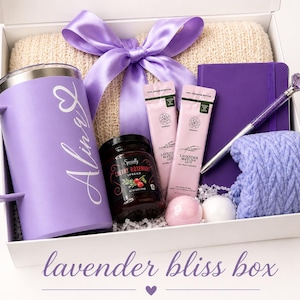 May include: A gift box filled with lavender-themed items. Includes a purple mug with a name, a jar of cherry rosemary spread, two tubes of lavender matcha latte, a purple notebook, a pen, a ball of yarn, and a bow.