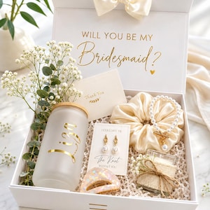 May include: A white gift box with a satin bow containing a frosted glass tumbler with the name Liza in gold, a pearl bracelet, a scrunchie, gold pearl earrings on a card reading I Couldn't Tie The Knot Without You, and a small candle.