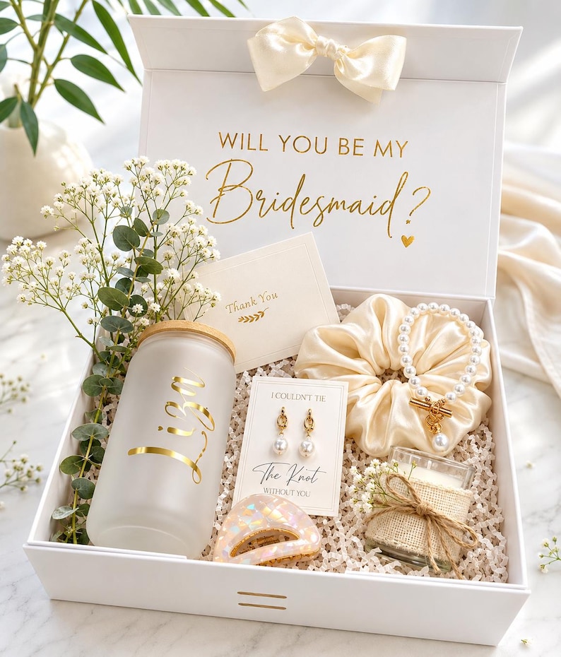 May include: A white gift box with a satin bow containing a frosted glass tumbler with the name Liza in gold, a pearl bracelet, a scrunchie, gold pearl earrings on a card reading I Couldn't Tie The Knot Without You, and a small candle.