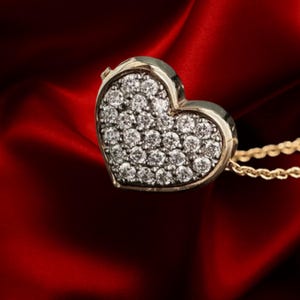 May include: A gold heart-shaped pendant necklace with a pave of small, sparkling diamonds. The pendant is set against a deep red, silky background, highlighting the jewelry's elegance and design.