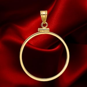 May include: A gold-colored pendant with a circular frame and a bail for a chain. The pendant is set against a deep red satin background, highlighting its metallic sheen. The design is simple and elegant.