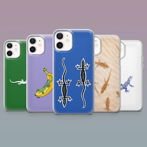 May include: A selection of phone cases with different designs. The cases display illustrations of a lizard, a banana, and other lizards. The cases are in shades of green, purple, blue, tan, and white. The cases are made of a clear, protective material.