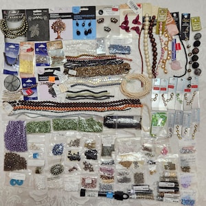 May include: A collection of jewelry-making supplies, including beads, pendants, and charms. Various colors and sizes of beads are visible, along with packaged pendants and charms. The image showcases a variety of materials for crafting necklaces, bracelets, and earrings.