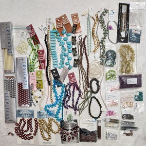 May include: A collection of assorted craft beads and jewelry supplies, including strands of turquoise, pearl, metallic, and glass beads in various shapes and sizes, along with several small plastic bags containing loose seed beads and findings.