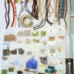 May include: A collection of assorted craft beads including loose strands of crystal, glass, and stone beads in various colors, shapes, and sizes, alongside numerous small plastic bags filled with individual beads and several retail bead display cards.