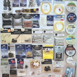 May include: A collection of jewelry making supplies including various metal chains, memory wires, elastic cords, and assorted findings like clasps, jump rings, and decorative charms packaged on individual cards and in small plastic bags for crafting.