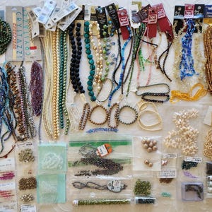 May include: A large collection of assorted jewelry making supplies including numerous strands of colorful glass, pearl, and metallic beads, various loose beads in plastic bags, and several packaged bead sets with brand labels like Crystazzi and Jewelry Designer.