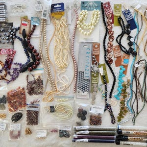 May include: A large collection of assorted jewelry making supplies including various strands of beads, pearls, and crystals on display cards, loose beads in plastic bags, and several long tubes filled with small seed beads in assorted colors and finishes.