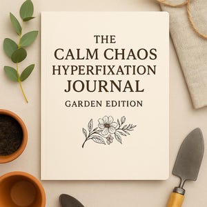 Op de afbeelding: Een crèmekleurig notitieboek met de titel "The Calm Chaos Hyperfixation Journal Garden Edition" met een bloemenillustratie. Het notitieboek is omgeven door tuingereedschap, een kleine pot en een takje groen.