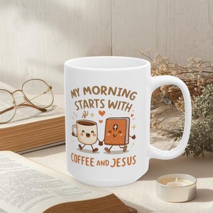 Puede incluir: Taza de cerámica blanca con el texto "MY MORNING STARTS WITH COFFEE AND JESUS". La taza presenta una taza de café de dibujos animados y una biblia tomados de la mano. Un par de gafas y un libro están en el fondo.