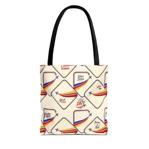 Könnte beinhalten: Eine cremefarbene Tragetasche mit schwarzen Henkeln und einem wiederkehrenden Muster aus Reiseemblemen im Retro-Stil. Jedes Emblem zeigt ein kleines Flugzeug mit einem roten, orangen und blauen Schweif sowie die Texte Catch Flights, Blue Skies, Good Vibes, Since 1971, Let's Go und Born to Fly.