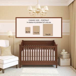 May include: A white crib with a brown wooden frame and a white mattress. A white armchair with a beige cushion is in the foreground. A framed poster on the wall shows three different canvas sizes in inches: 8x10, 11x14, and 16x20. The text on the poster reads "Canvas Size - Portrait in relation to standard 54" crib size".