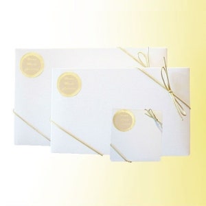 May include: Three white gift boxes of different sizes tied with a thin, gold ribbon. The boxes have a gold circle sticker with the text "Thank You" on them.