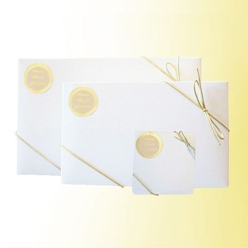 May include: Three white gift boxes of different sizes tied with a thin, gold ribbon. The boxes have a gold circle sticker with the text "Thank You" on them.