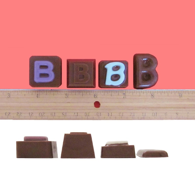 May include: Four chocolate blocks spelling out the word "BBB" with a ruler in the background. The first "B" is purple, the second and third "B" are brown, and the last "B" is white.