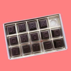 May include: A white box filled with dark chocolate squares, each with a letter spelling out "DARK CHOCOLATE LOVER".
