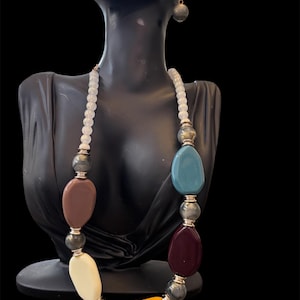 May include: A colorful necklace and matching earrings set. The necklace features large, irregularly shaped beads in shades of brown, cream, blue, burgundy, and yellow, interspersed with gray and white beads. The earrings are small, round gray beads.
