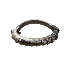 May include: A silver-toned bracelet with a snake-like design. The bracelet features articulated, scale-like segments that curve around the wrist. The band is made of a flexible, woven metal.