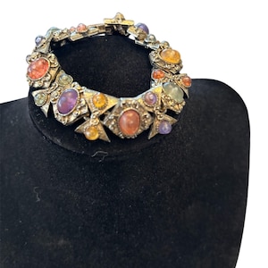 May include: A silver-toned metal link bracelet featuring a series of geometric segments. Each segment is set with smooth, oval-shaped cabochon stones in various colors including orange, purple, yellow, and light green, with a secure clasp closure.
