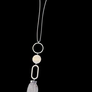 May include: Silver-toned necklace with a long chain and a series of geometric pendants. The design includes a large circle, a circular pendant, an elongated oval, and a tassel at the bottom. The necklace is displayed against a black background.