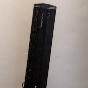 May include: A black, smooth, rectangular crystal point with a slightly rounded top.