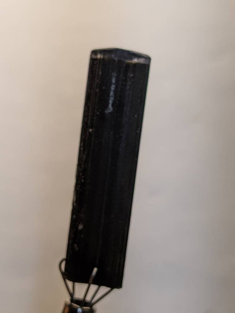 May include: A black, smooth, rectangular crystal point with a slightly rounded top.