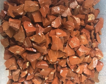 May include: A close-up view of a container filled with a large quantity of small, irregularly shaped, red-brown jasper stones.