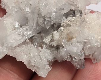 May include: A cluster of clear quartz crystals with a rough, natural texture. The crystals are clustered together in a dense formation, creating a visually interesting and unique piece.
