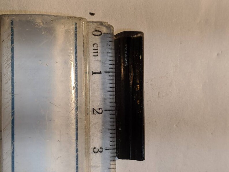 May include: A black metal object measuring approximately 2.5 cm in length. The object is rectangular in shape and has a slightly rounded edge.
