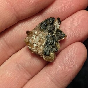 May include: A small, irregularly shaped, brown and black crystal with a rough, textured surface.